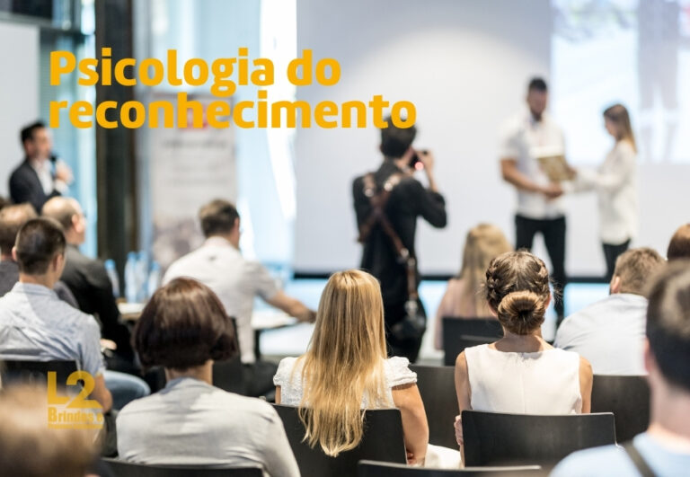 Pessoas assistindo a uma apresentação onde uma pessoa recebe um prêmio, com o texto "Psicologia do reconhecimento" sobreposto na imagem.