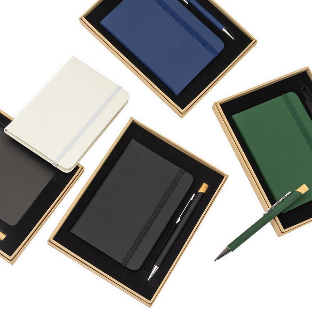 brinde-executivo-com-caderno-e-caneta-premium Visão superior de vários kits de brinde executivo com caderno e caneta em cores sortidas (azul, preto, verde, branco), destacando a apresentação do produto.